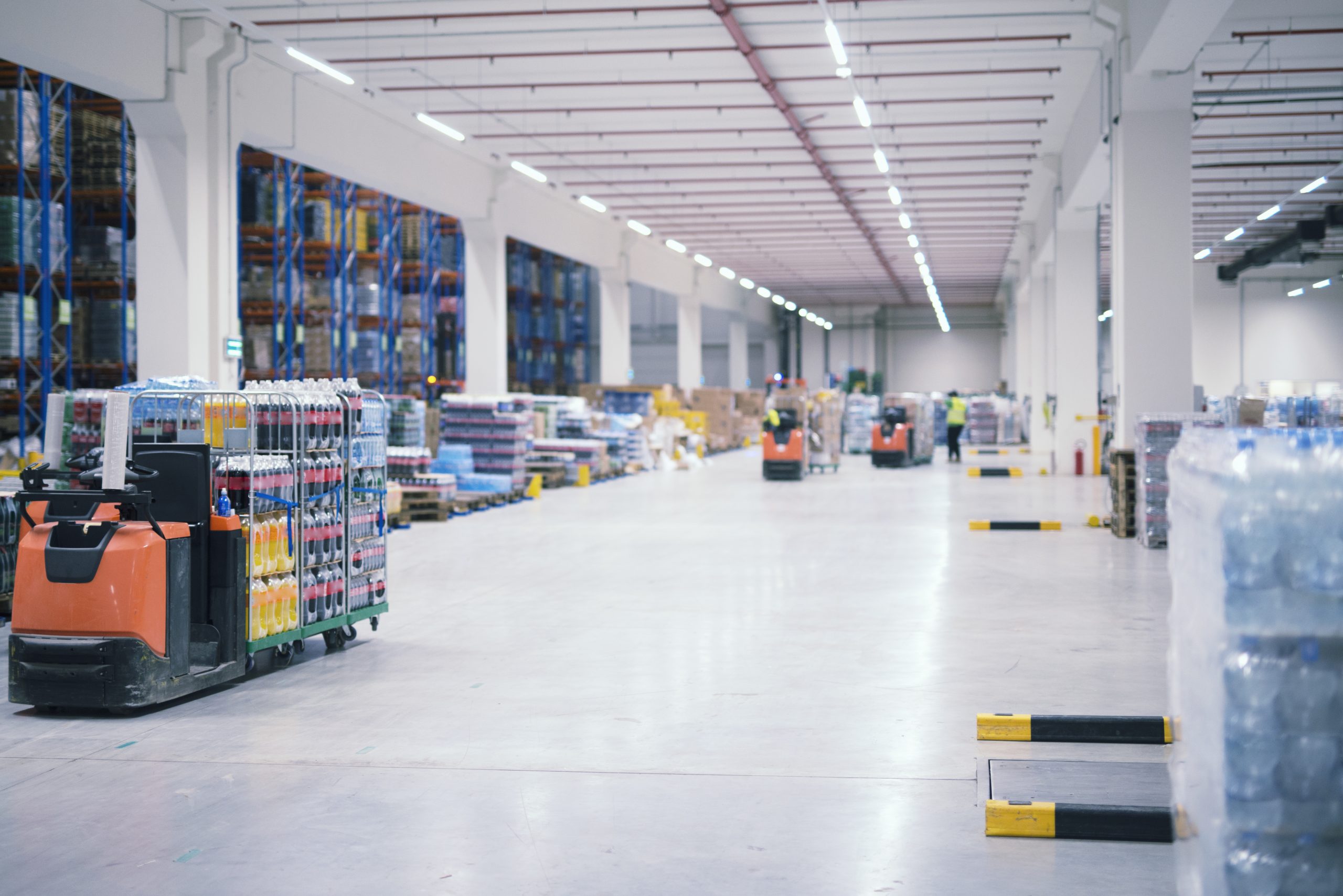 Warehouse industrial building interior with people and forklifts handling goods in storage area.